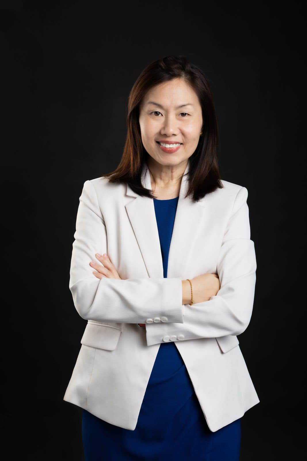 Gladys Ng smiling with her arms folded, wearing a cream blazer over a navy dress