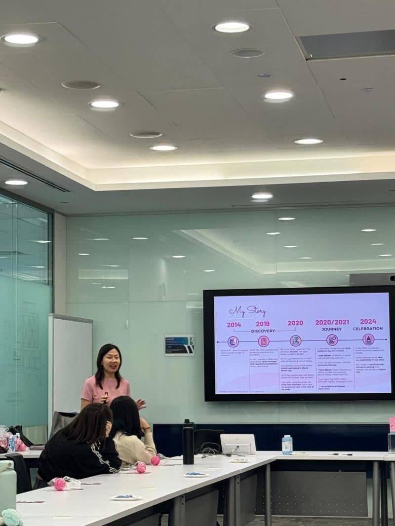 Gladys, in pink, talking with attendees at a meeting table in front of her story timeline
